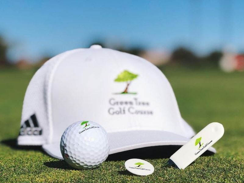 Green Tree Golf Course branded golf ball, tee, marker, and hat on the green.